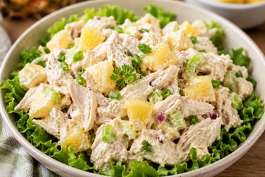 A creamy chicken salad with pineapple chunks, celery, and green onions served on a bed of fresh lettuce.