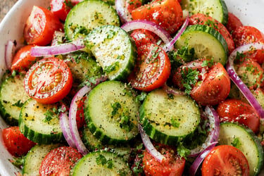 Fresh cucumber tomato salad with red onions and herb vinaigrette dressing in a white bowl.