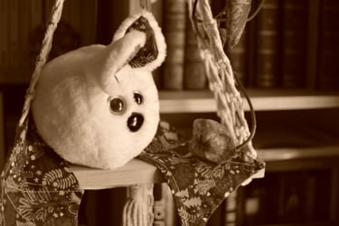peluche artisanale suspendue devant des livres, regard expressif tourné vers l’avant