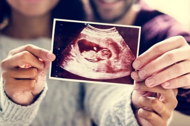 A smiling couple holding up an ultrasound baby scan photo to announce a pregnancy.