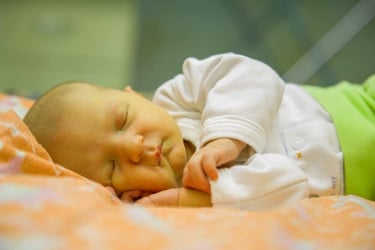 A peaceful newborn baby with jaundice sleeping soundly on a patterned orange and white blanket.