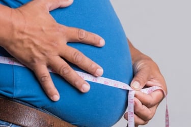 A man in a blue shirt uses a measuring tape to check his waist size for weight loss tracking.