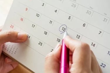 A person circles a date on a desk calendar with a pink pen for appointment scheduling.