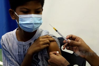 A young boy wearing a face mask receives a medical vaccination injection in his upper arm.