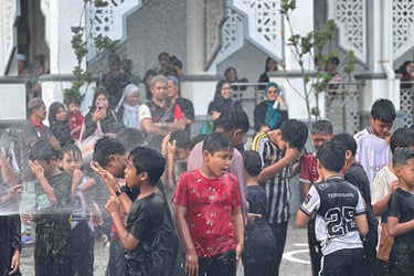 Young boys playing in water spray outside a mosque with traditional Islamic architecture.