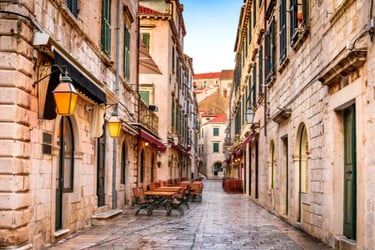 Empty outdoor restaurant seating in a narrow stone alleyway in Dubrovnik Old Town, Croatia.