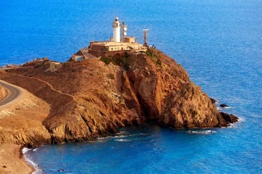 Cabo de Gata lighthouse perched on a rocky cliff overlooking the blue Mediterranean Sea in Almeria, Spain.