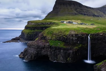 Mulafossur Waterfall cascading from green cliffs into the ocean near Gasadalur village, Faroe Islands.