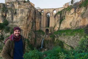 A man smiling in front of the historic Puente Nuevo bridge and El Tajo gorge in Ronda, Spain.