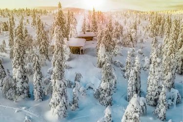 Cozy wooden cabin nestled in a snowy winter forest at sunset with frost-covered trees.