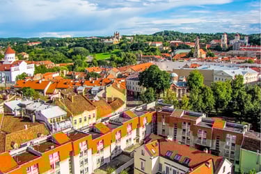 Panoramic view of Vilnius Old Town with orange terracotta rooftops, historic churches, and lush green hills.