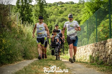 Two runners pushing a child in a racing wheelchair during an outdoor inclusive trail running event.