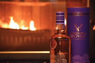 A bottle and cask of Gordon & Macphail single malt scotch whisky in front of a fireplace