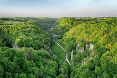 Aerial view of a lush green valley with limestone cliffs and a winding road through a dense forest.