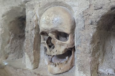 Real human skull embedded in a stone wall at an ancient historical catacomb or ossuary site.