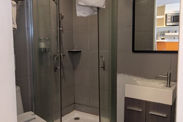 Modern compact bathroom featuring a corner glass shower, white toilet, and dark wood vanity with a square sink.