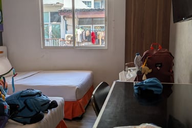A budget hostel room with twin beds, air conditioning, and a view of a city window.