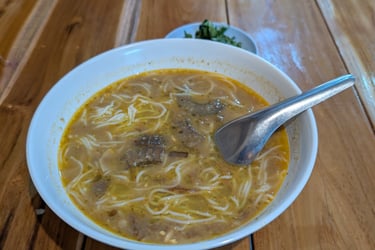 Traditional Myanmar fish curry soup served in a white bowl on a rustic wooden table.