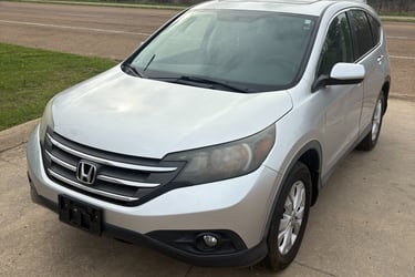 Silver Honda CR-V compact SUV parked on a concrete driveway with trees in the background.