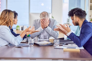 Stressed senior manager covering his face during a tense business meeting with diverse colleagues arguing.