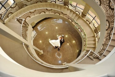 a bride and groom walking down a spiral staircase