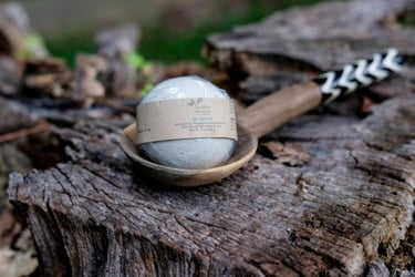 a light green round bath bomb on a wooden spoon on a tree stump