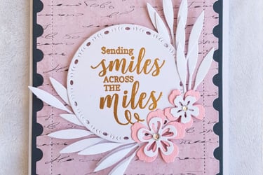 Greeting card with the message "Sending smiles across the miles" in gold on a round white cutout. Pi