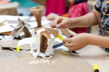 A child's hands glueing a piece of paper to a cardboard structure.