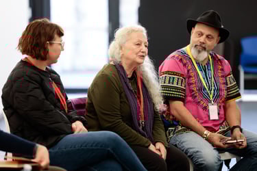Three people seated on chairs. The person in the middle is speaking and the other two listen closely