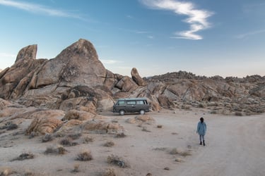 A van parked in near a small mountain and a person walking towards it.