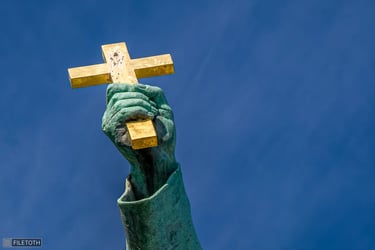 Hand lifting the cross skyward, metal glowing in direct sunlight.