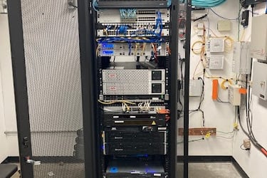 Open server rack with network switches, patch panels, and power supply units in a data center room.