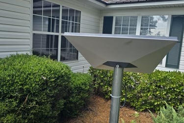 A rectangular Starlink satellite internet dish mounted on a pole outside a residential white house.
