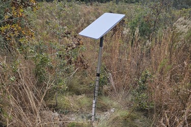 A Starlink satellite dish mounted on a pole in a rural field for remote internet access.