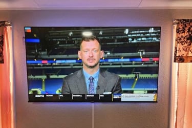 A wall-mounted smart TV with LED backlighting displays a sports broadcast in a living room setup.