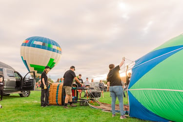 A flight crew prepares colorful hot air balloons for takeoff in a grassy field during a festival.