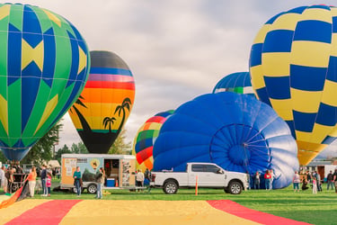 Colorful hot air balloons inflating at an outdoor festival with spectators and a white pickup truck.