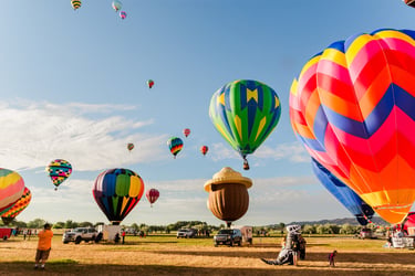 Colorful hot air balloons taking off from a field during a morning festival under a clear blue sky.