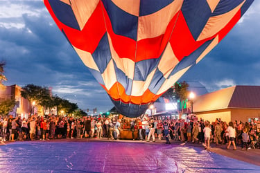 A colorful hot air balloon inflating over a crowded city street during a festive evening event.