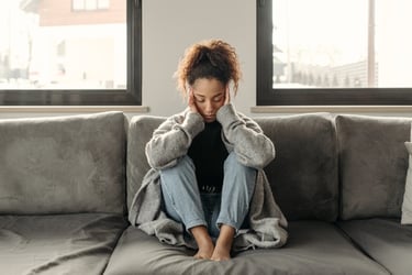 A stressed woman sitting on a couch holding her head, illustrating mental health and anxiety relief.