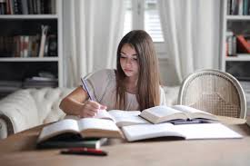 Young woman doing research at a desk with several books open.