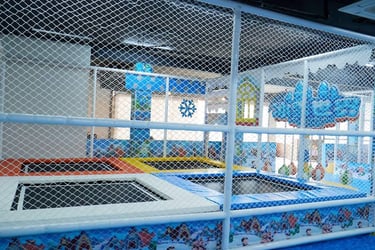 Indoor kids trampoline park with safety netting and winter-themed padding for children's play area.