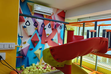 Indoor kids play area with a colorful rock climbing wall, red slide, and foam pit for children.