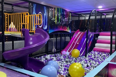 Indoor soft play area featuring a purple spiral slide, ball pit, and colorful climbing structures for kids.