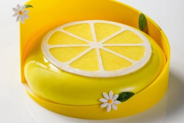 Gourmet lemon mousse cake with a yellow mirror glaze, citrus slice topper, and white fondant daisies.