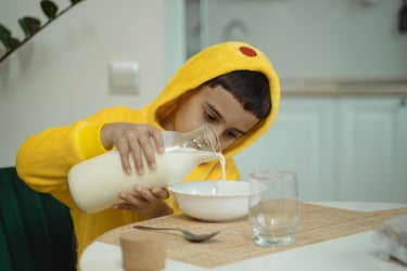 Bambino versa il latte in una ciotola durante la colazione