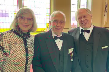 a smiling woman in a norwegian sweater stands next to two smiling men in tuxedos