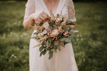 Eine Braut in einem Spitzenhochzeitskleid hält einen rustikalen rosa Blumenstrauß mit Eukalyptus