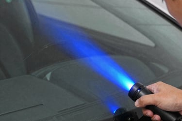 Technician uses a handheld UV lamp to cure resin during a professional car windshield chip repair.