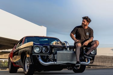 don abenante sits on a custom turbocharged muscle car with an exposed front intercooler at sunset.